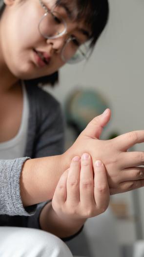 Een vrouw kijkt naar haar hand en drukt met haar andere hand op die hand