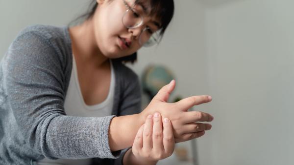 Een vrouw kijkt naar haar hand en drukt met haar andere hand op die hand