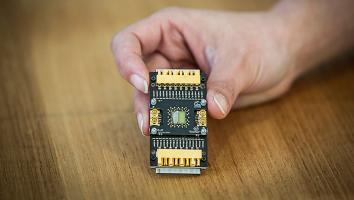 Een hand houdt een rechthoekige printplaat van een paar centimeter vast waar een qubit op zit