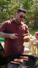 Drie mannen staan naast een barbecue broodjes met hotdogs te maken en te drinken en te kletsen