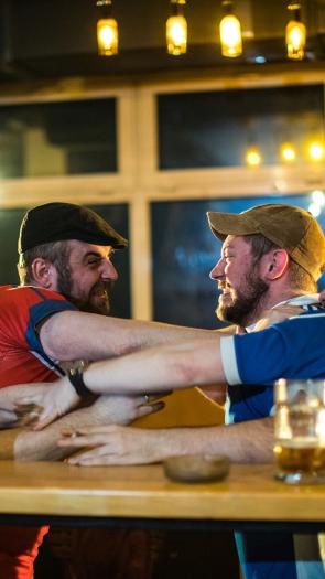 Mannen in een kroeg in blauwe en rode shirts staan boos tegenover elkaar en grijpen elkaars shirt vast