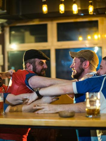 Mannen in een kroeg in blauwe en rode shirts staan boos tegenover elkaar en grijpen elkaars shirt vast