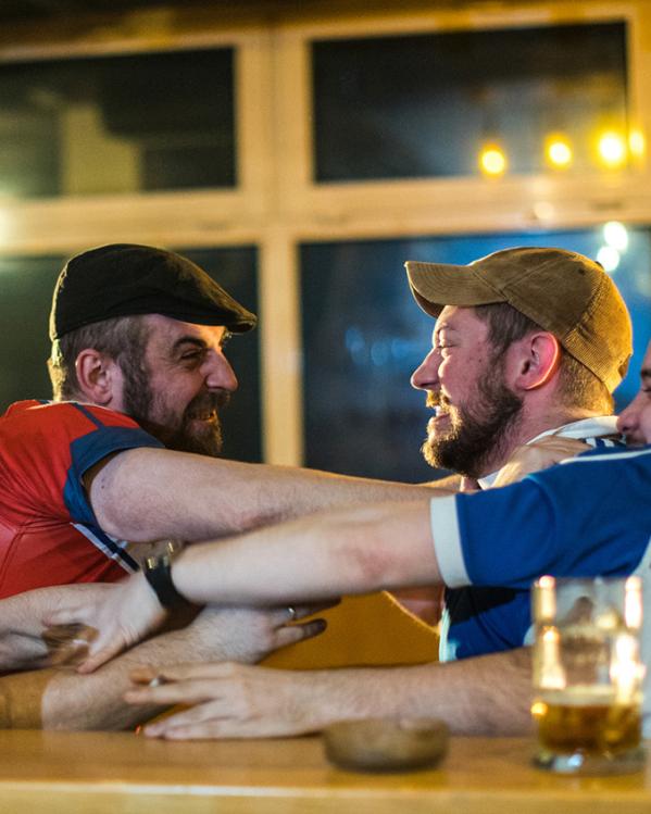 Mannen in een kroeg in blauwe en rode shirts staan boos tegenover elkaar en grijpen elkaars shirt vast
