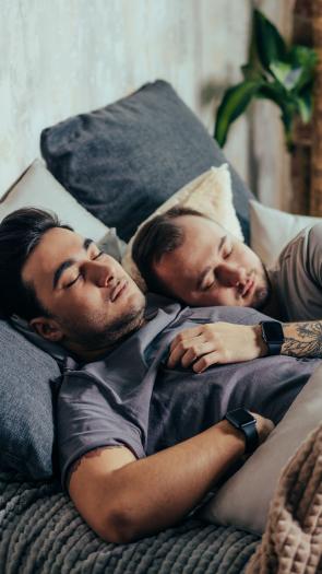 Twee mannen slapen samen in bed, de een ligt met zijn hand op de ander zijn borst
