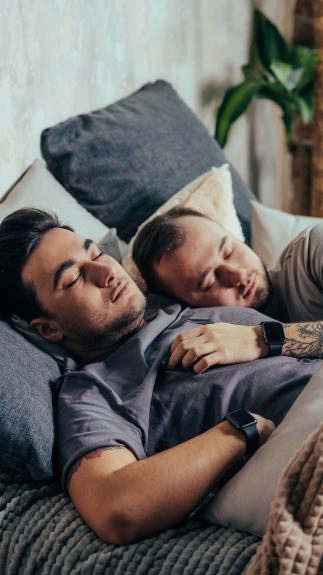 Twee mannen slapen samen in bed, de een ligt met zijn hand op de ander zijn borst