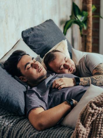 Twee mannen slapen samen in bed, de een ligt met zijn hand op de ander zijn borst