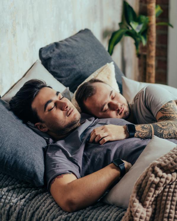 Twee mannen slapen samen in bed, de een ligt met zijn hand op de ander zijn borst