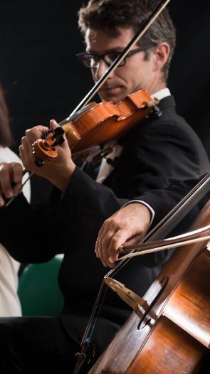 Leden van een orkest spelen op hun instrumenten: een cello, viool en fluit op een rij met een donkere achtergrond