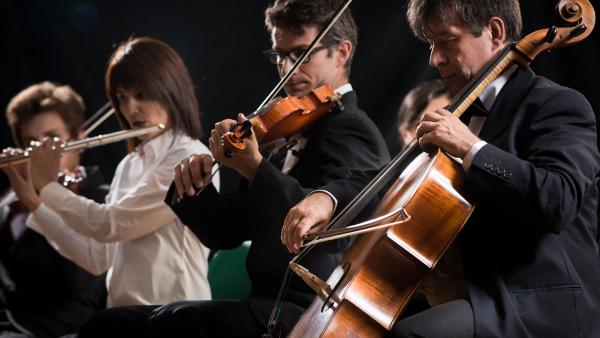 Leden van een orkest spelen op hun instrumenten: een cello, viool en fluit op een rij met een donkere achtergrond