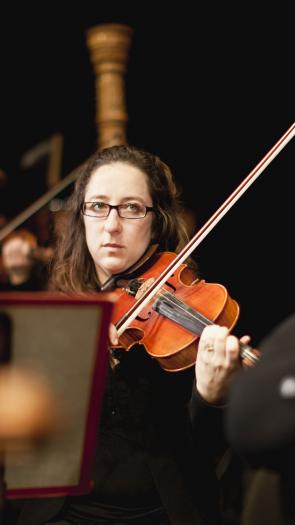 Leden van een orkest spelen op de viool, met één vrouw duidelijk in het midden uitgelicht