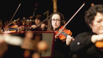 Leden van een orkest spelen op de viool, met één vrouw duidelijk in het midden uitgelicht