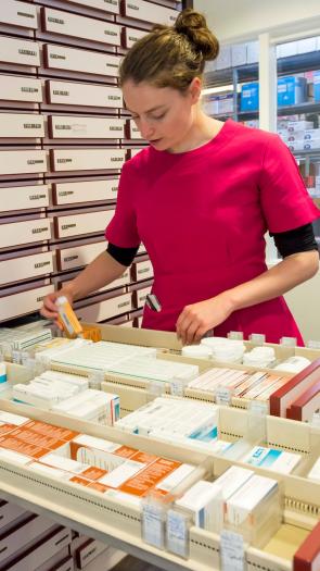 Een apothekersassistent zoekt medicijnen in een lade bij de apotheek