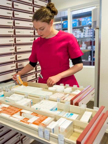 Een apothekersassistent zoekt medicijnen in een lade bij de apotheek