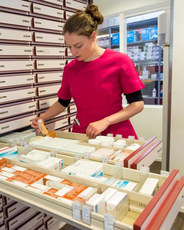 Een apothekersassistent zoekt medicijnen in een lade bij de apotheek