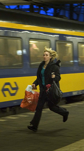 Vrouw met paardentaart in haar haar rent op perron naast wegrijdende NS trein