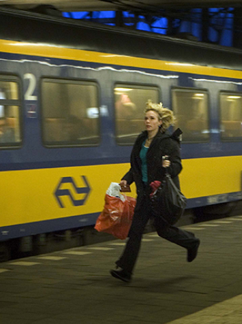 Vrouw met paardentaart in haar haar rent op perron naast wegrijdende NS trein