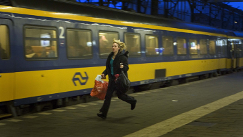 Vrouw met paardentaart in haar haar rent op perron naast wegrijdende NS trein