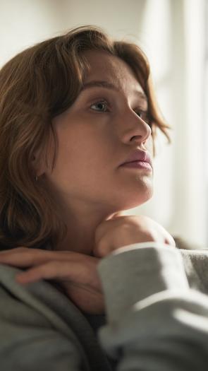Een vrouw staart somber voor zich uit, zittend op de bank 