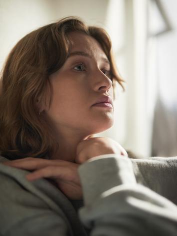 Een vrouw staart somber voor zich uit, zittend op de bank 