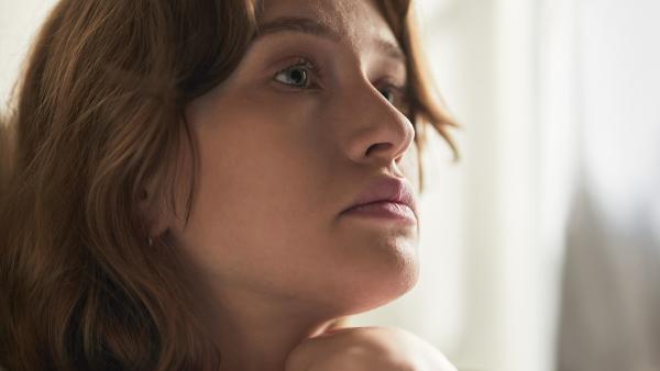 Een vrouw staart somber voor zich uit, zittend op de bank