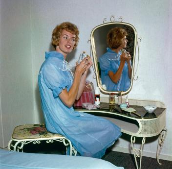 Zangeres Ria Valk (1941) in een blauwe nachtjapon achter haar kaptafel met spiegel, met een flesje parfum in haar handen, Nederland 1962.