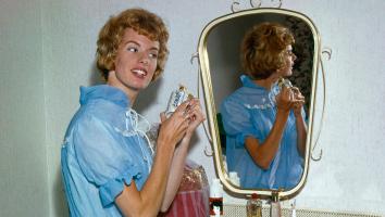 Zangeres Ria Valk (1941) in een blauwe nachtjapon achter haar kaptafel met spiegel, met een flesje parfum in haar handen, Nederland 1962.