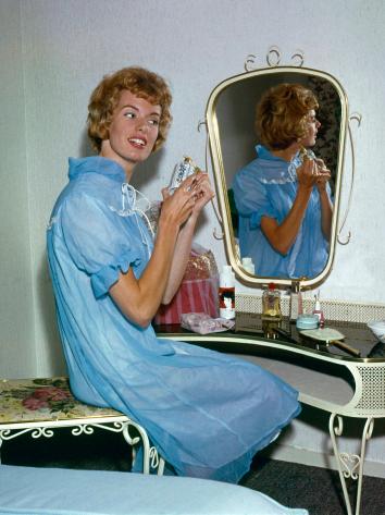 Zangeres Ria Valk (1941) in een blauwe nachtjapon achter haar kaptafel met spiegel, met een flesje parfum in haar handen, Nederland 1962.
