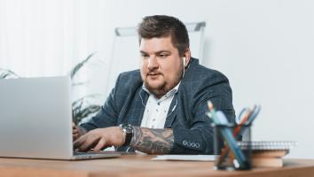 een man met overgewicht zit te werken achter zijn bureau op zijn laptop