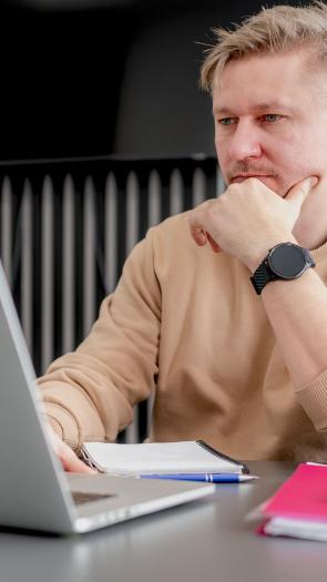 een man zit nadenkend met zijn hand onder zijn kin achter zijn laptop