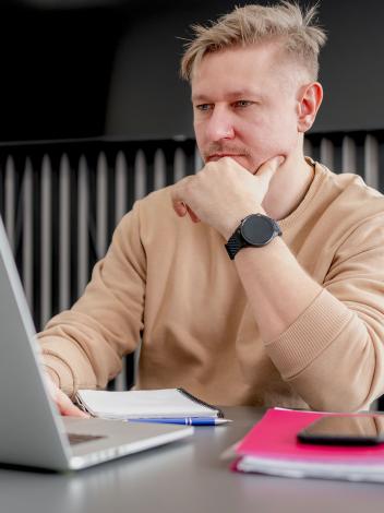 een man zit nadenkend met zijn hand onder zijn kin achter zijn laptop