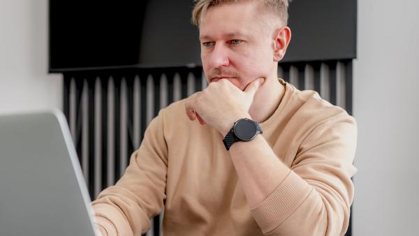 een man zit nadenkend met zijn hand onder zijn kin achter zijn laptop