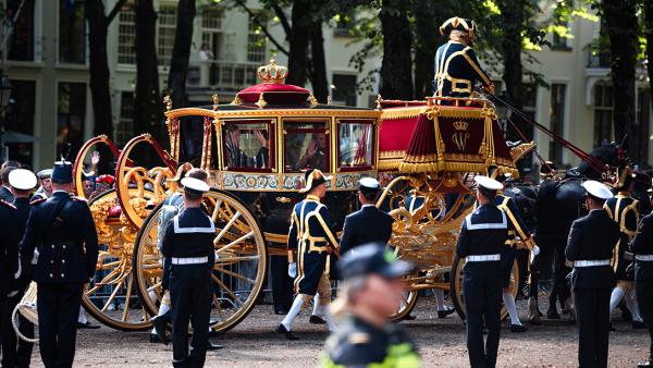 Glazen koets met zwaaiend koningspaar rijdt over straat