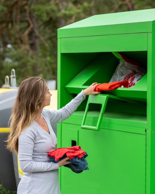 Vrouw stopt losse kledingstukken in de klep van een grote textielbak.