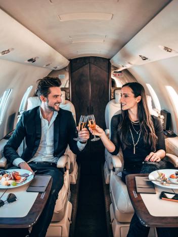 Een man en vrouw proosten samen met champagneglazen in hun privéjet.