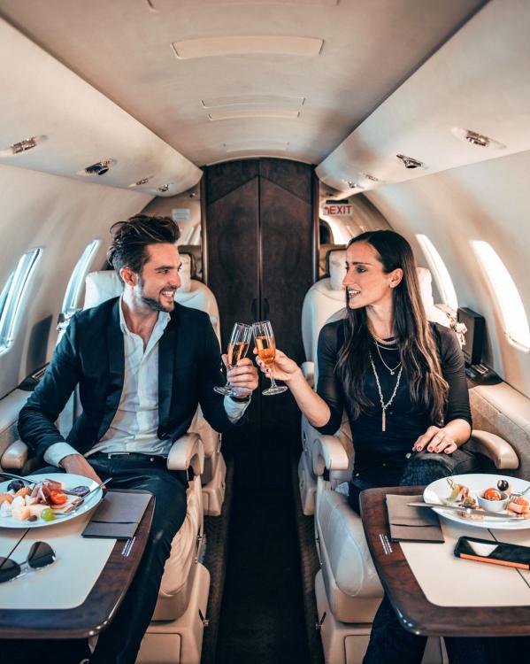 Een man en vrouw proosten samen met champagneglazen in hun privéjet. 