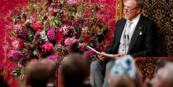 Willem Alexander zit met papier in zijn handen en leest de troonrede voor