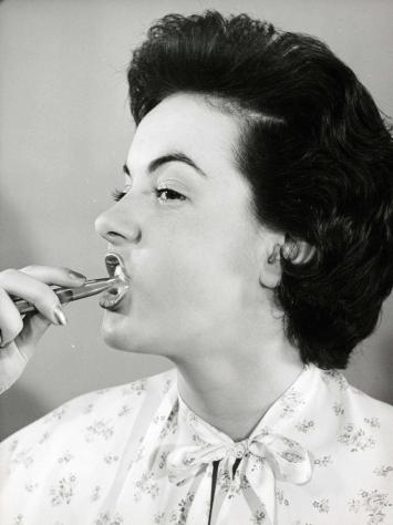 Een zwart-witfoto van een vrouw die haar tanden poetst in de jaren 1950.