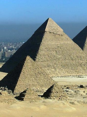 De piramides van Gizeh, een foto van een grotere piramide op de achtergrond en een kleinere op de voorgrond, met daarachter een grote stad.