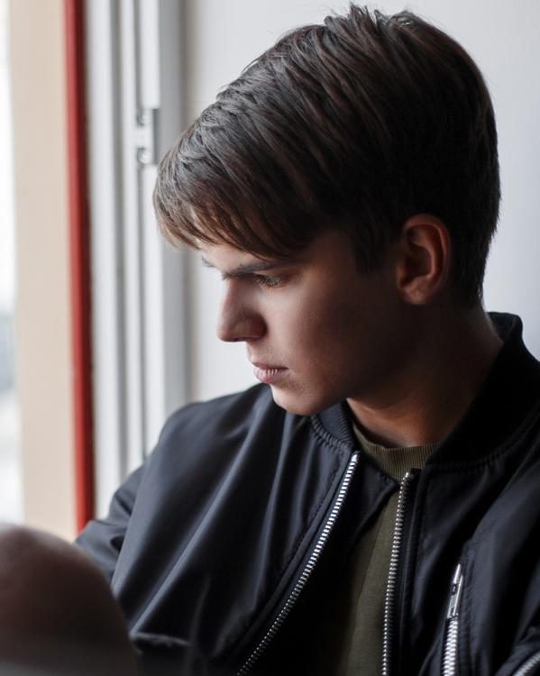 een puberjongen zit in de vensterbank en staart uit het raam