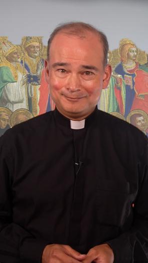 Een priester staat voor een afbeelding van allerlei verschillende heiligen binnen het christendom