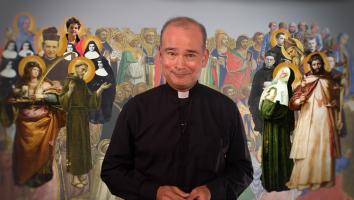 Een priester staat voor een afbeelding van allerlei verschillende heiligen binnen het christendom