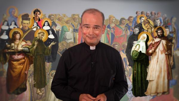 Een priester staat voor een afbeelding van allerlei verschillende heiligen binnen het christendom