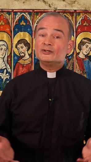 Een priester staat voor een afbeelding van allerlei verschillende heiligen binnen het christendom