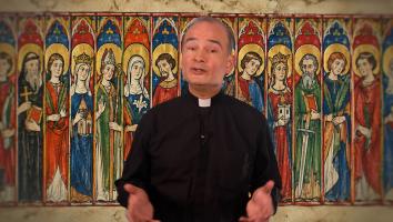 Een priester staat voor een afbeelding van allerlei verschillende heiligen binnen het christendom