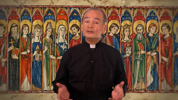 Een priester staat voor een afbeelding van allerlei verschillende heiligen binnen het christendom