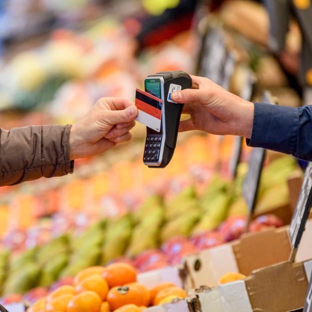 Iemand rekent af met de pinpas bij een mobiel pinautomaat op de markt, met op de achtergrond de marktkraam van de groenteboer